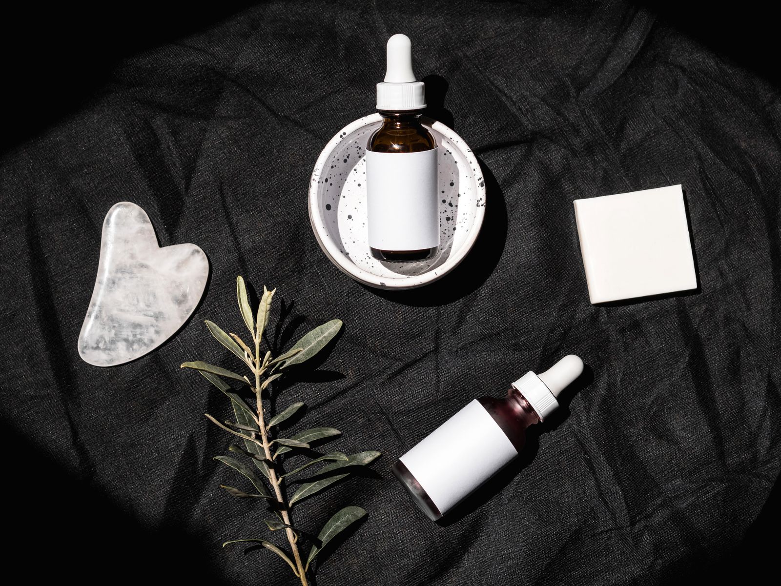 Flacons de soin et accessoires disposés sur un textile sombre